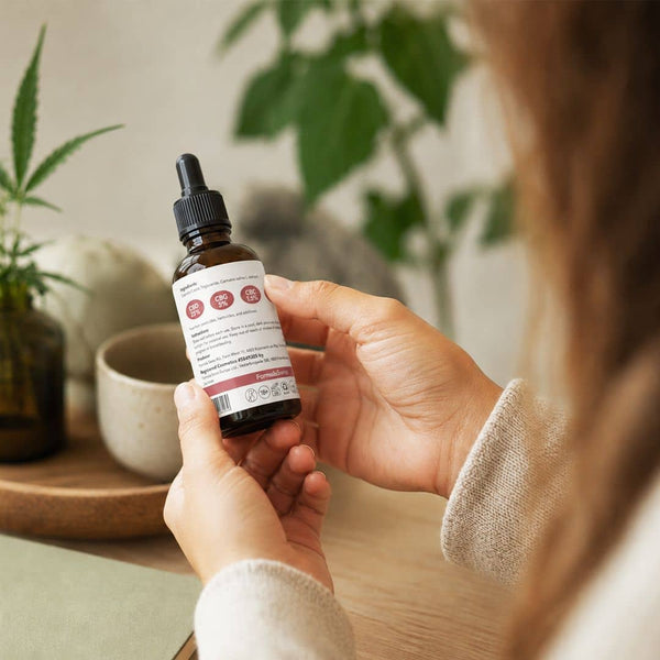 Kvinne som gransker produktetiketten på en Formula Swiss cannabinoidolje i naturlige innendørsomgivelser.